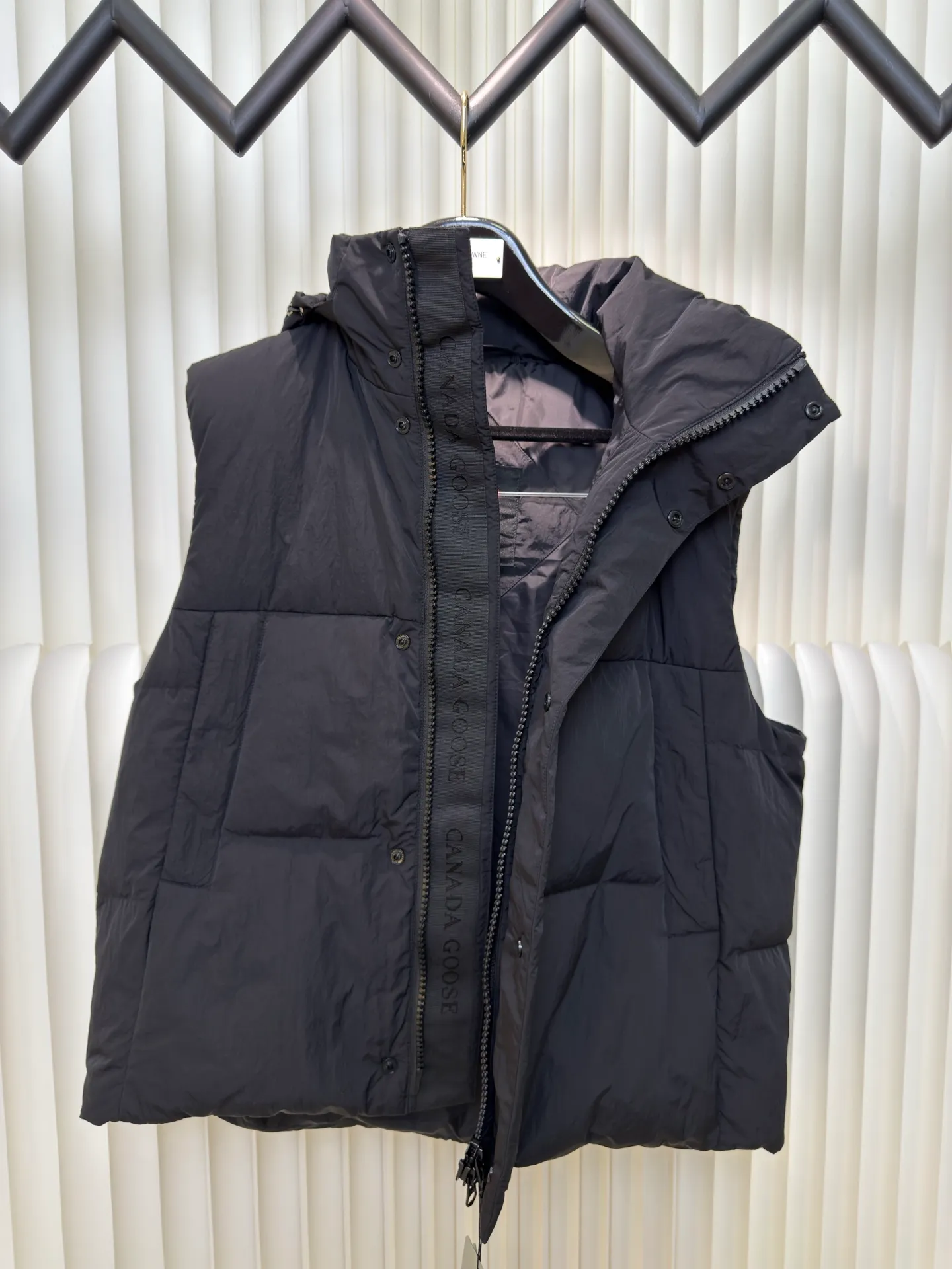 P760 Big Goose Logo Hooded Down Vest is made of high-quality protective nylon fabric, which not only enhances the wear resistance of the surface, but also takes into account wind resistance, ensuring excellent performance in various harsh weather conditions.  90 national standard high-quality white duck down: selected high-loft down, weighing 170g, light and warm, with excellent temperature locking performance and good resilience.  Three-dimensional quilting process: Precision thread reinforcement to prevent velvet drilling and ensure that the fluffy and resilient elasticity lasts as new.  Details: The ribbon is woven with polyester as the base. The brand letters are decorated on the ribbon through high-precision computer embroidery. The edges of the pattern are clear, the stitches are fine and even, and multiple layers of embroidery thread are stacked to enhance the three-dimensional effect. Size S M L XL